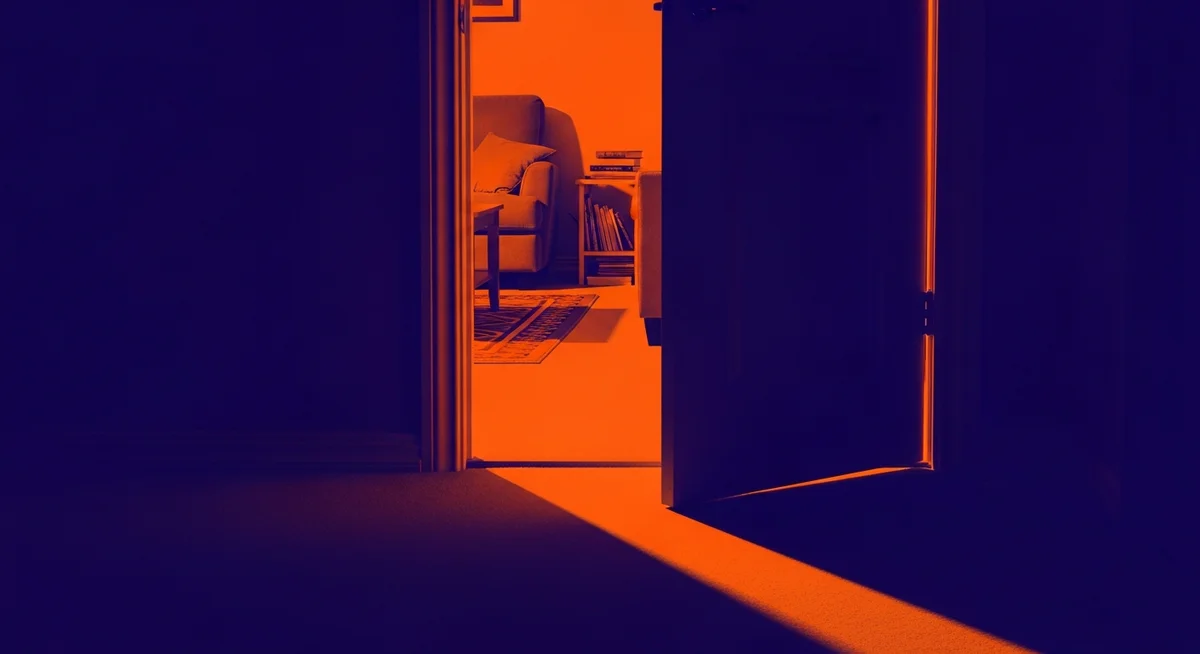 A duotone image of a slightly ajar interior doorway, with a dramatic shadow cast across the threshold into a cozy living space, suggesting a boundary being crossed.